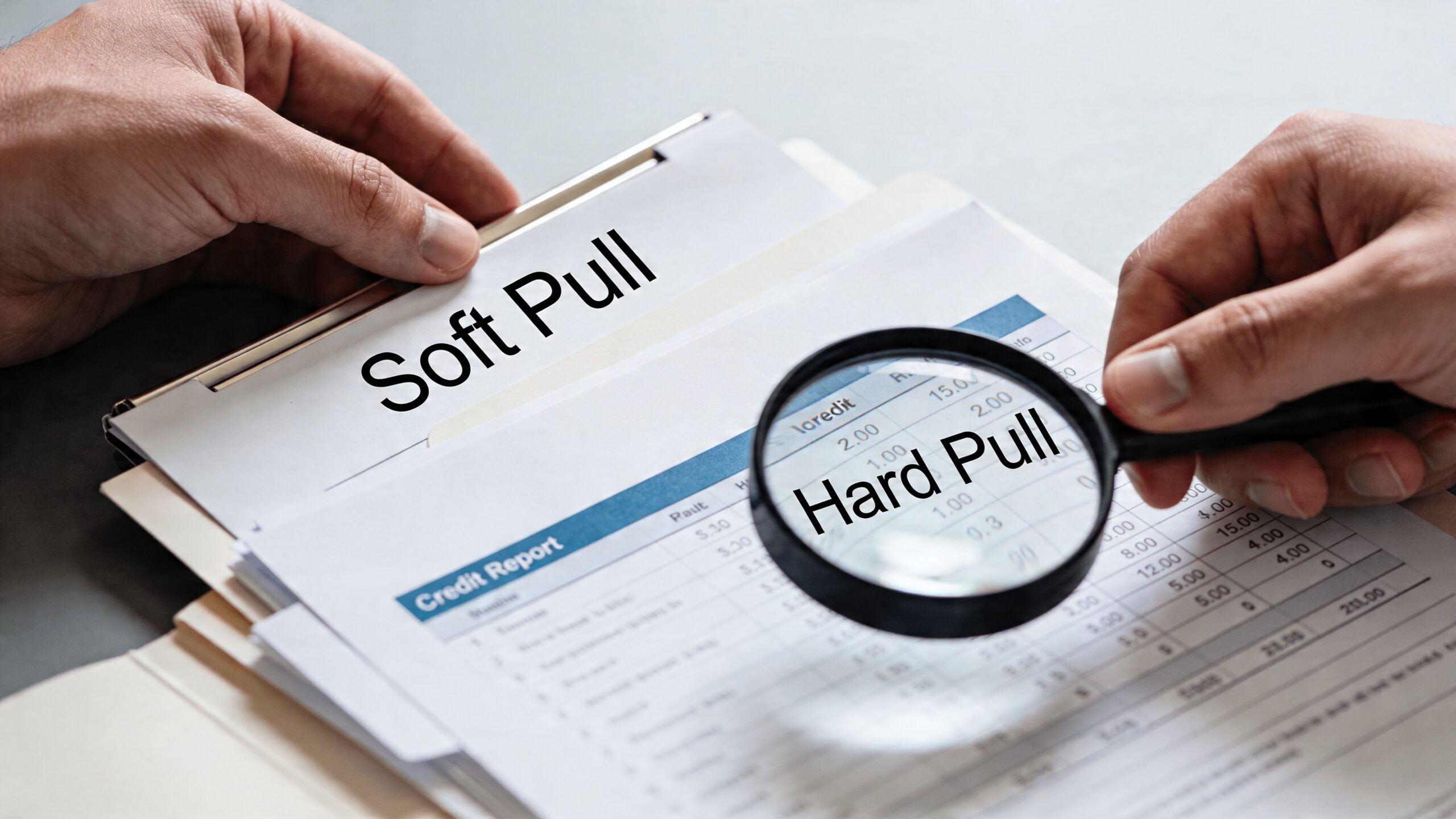 A person using a magnifying glass to examine a credit report comparing soft and hard pulls.
