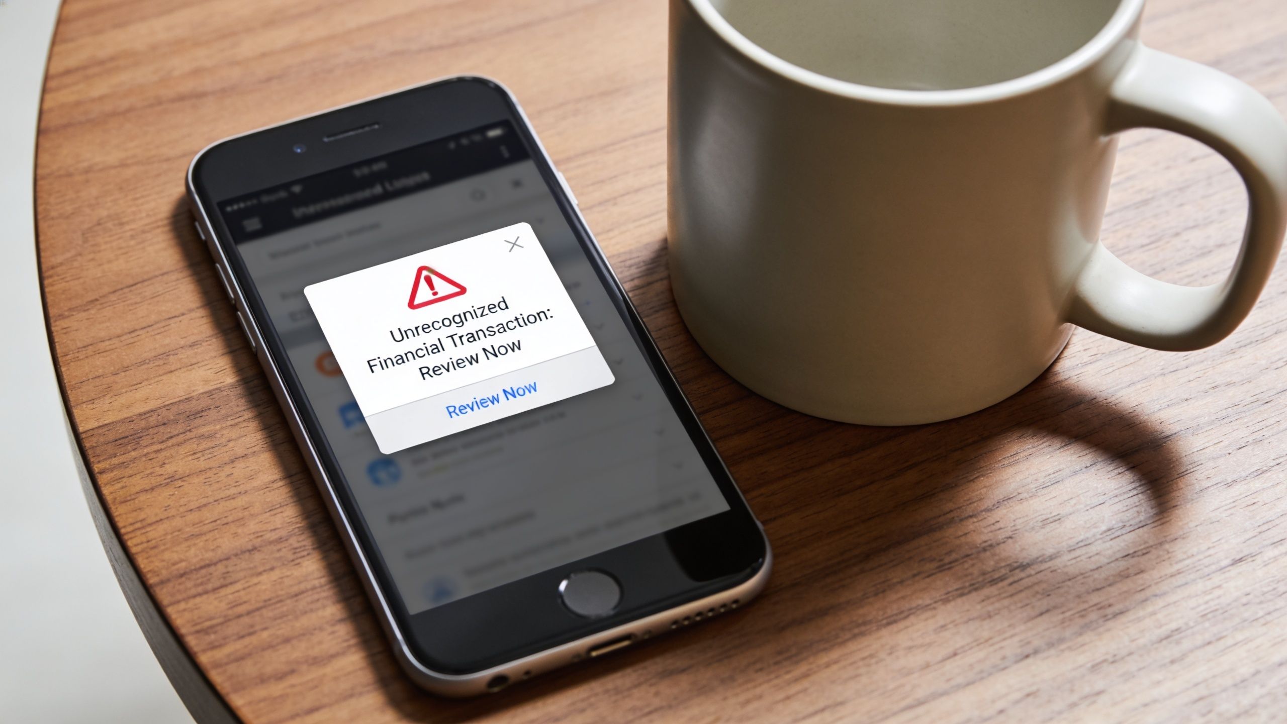 A smartphone resting on a wooden table displaying a financial transaction security alert warning pop-up notification.